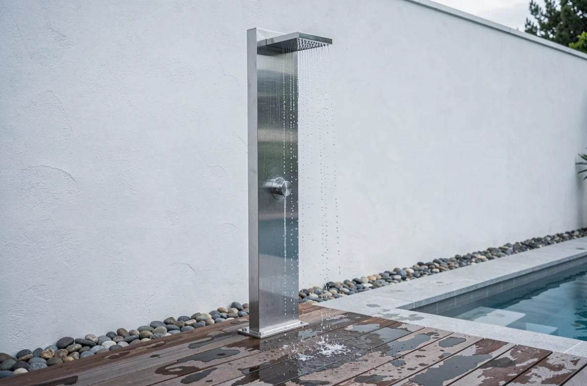 Douche extérieure en inox brossé avec pommeau pluie posée en bord de piscine sur terrasse en bois